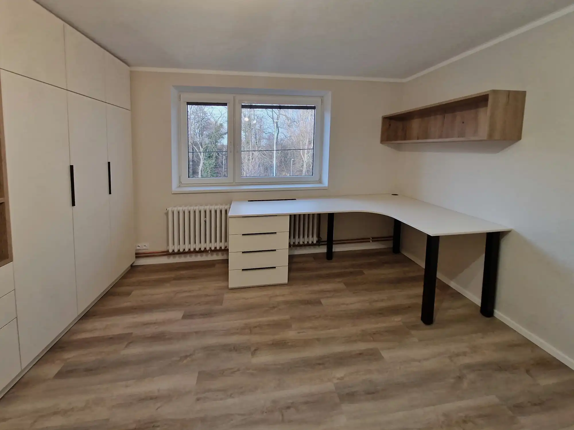 A small office with wood-look vinyl plank flooring running wall to wall beneath a corner desk
