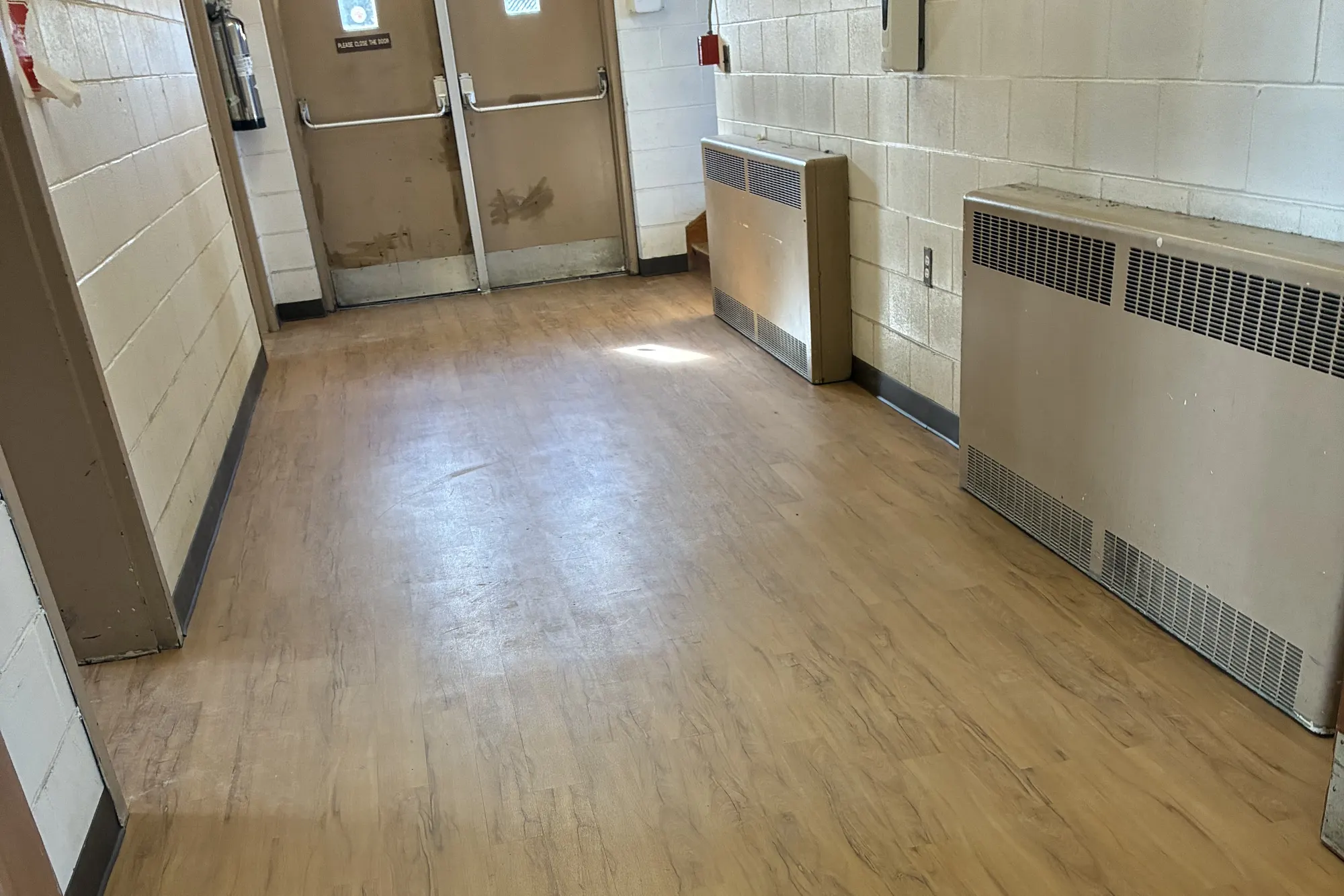 A building corridor with new wood-look vinyl plank running from the double exit doors past the wall heaters