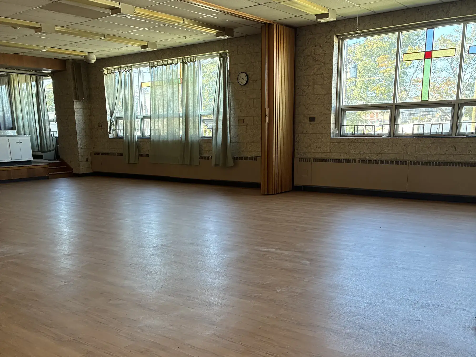 A large meeting hall with newly installed wood-look vinyl plank flooring running beneath tall windows