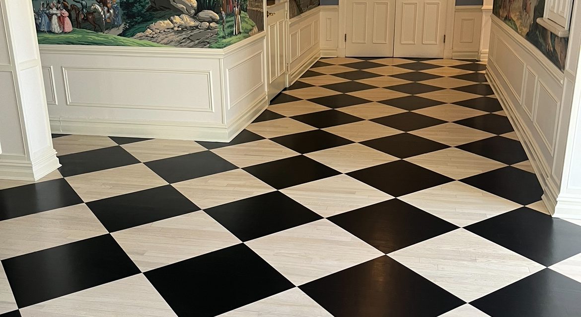 Custom black and white checkerboard hardwood floor in a paneled hallway