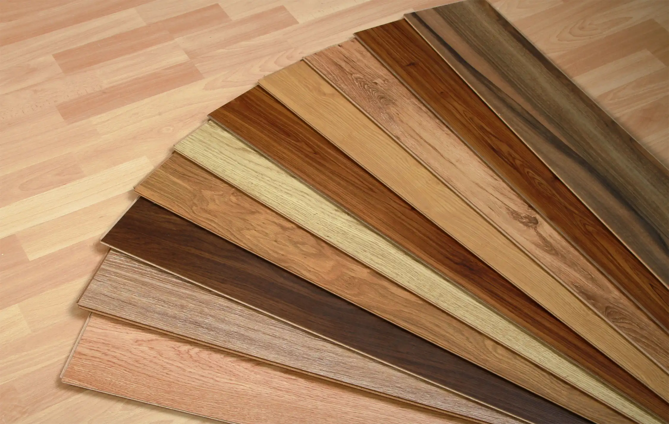 Laminate plank samples fanned out across a laminate floor, showing a range of wood tones and grains